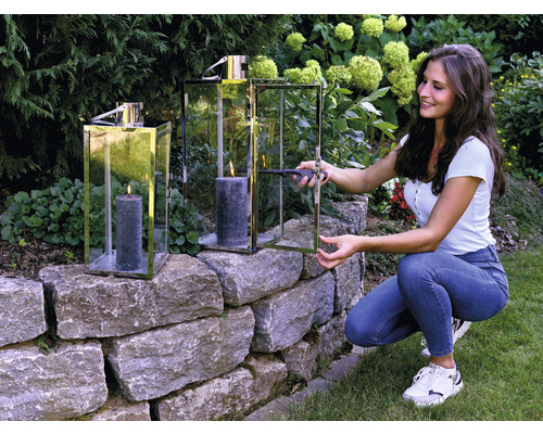 Frau zündet Kerze in Windlicht auf Steinmauer im Garten an