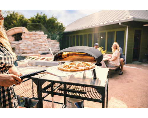 Dona Pizzaofen mit Pizza auf Pizzaschieber und Personen im Hintergrund