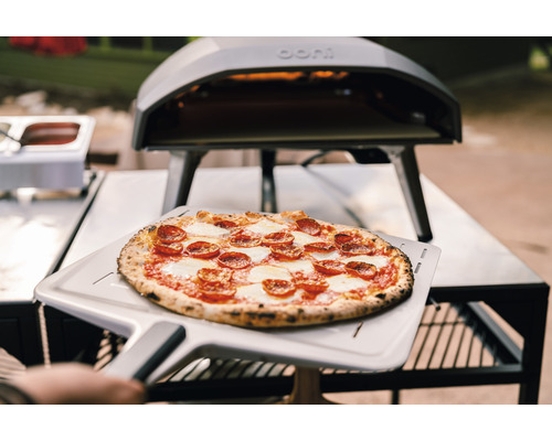 Pizza mit Salami und Mozzarella auf einem Pizzaschieber vor einem Pizzaofen.