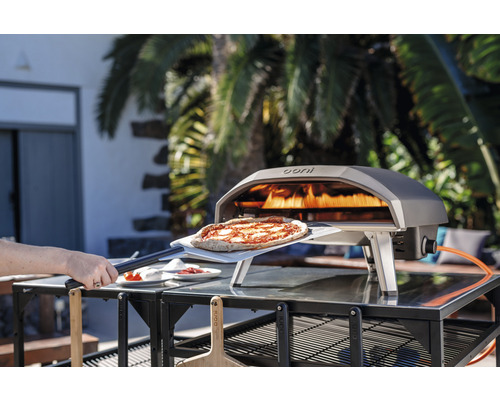 Ooni Pizzaofen mit Pizza auf Pizzaschieber im Außenbereich.