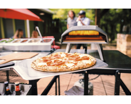 Szene mit Pizza auf Pizzaschieber und Pizzaofen im Außenbereich