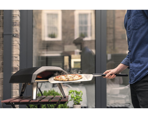 Eine Pizza wird mit einem Pizzaschieber aus einem Pizzaofen genommen.
