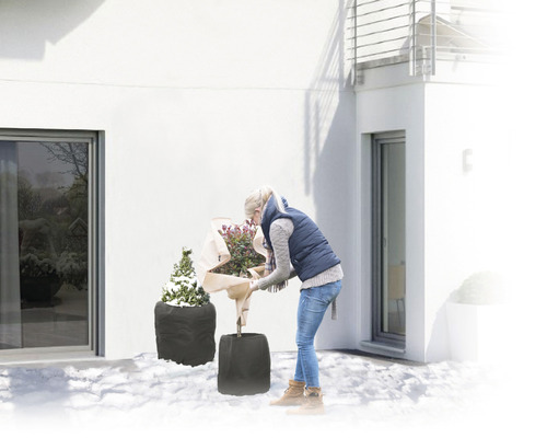 Frau verpackt Pflanzen mit Winterschutz im Garten.