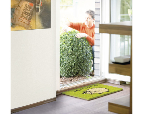 Szene mit einer Fußmatte mit Schafsmotiv und der Aufschrift Willkommen vor einer Haustür