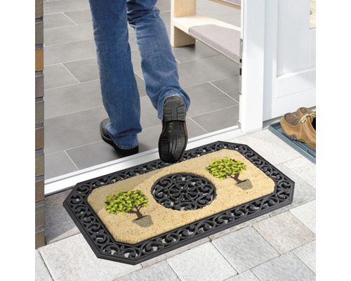 Fußabstreifer mit Pflanzenmuster und Zierelementen vor einer Haustür.