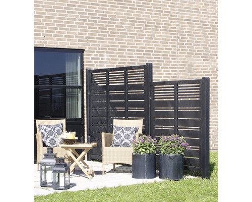 Terrasse mit Windschutzwand, Rattansesseln, Tisch, Laternen und Pflanzenkübeln vor einer Hauswand