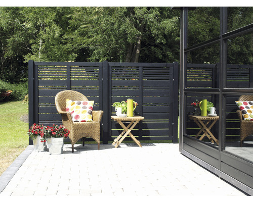 Gartenszene mit Holzzaun, Korbsessel, Beistelltisch und Blumen