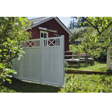 Weißer Gartenzaun mit Holztisch und rotem Haus im Hintergrund