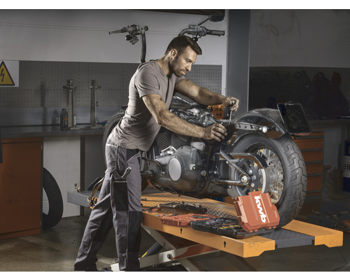 Mann repariert ein Motorrad in einer Werkstatt mit kwb Werkzeugkoffer