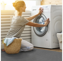 Frau bedient Waschmaschine auf einer grauen Fußmatte im Badezimmer