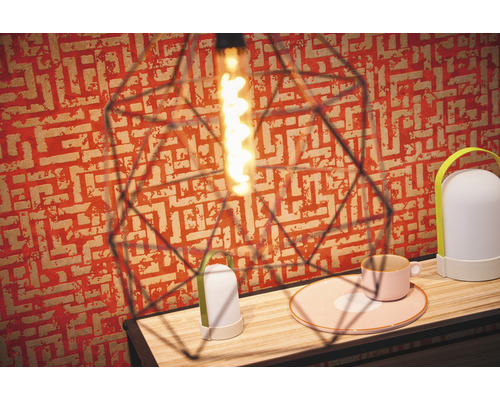 Innenaufnahme mit dekorativer Lampe, Tischleuchte und Geschirr auf einem Holztisch vor gemusterter Tapete