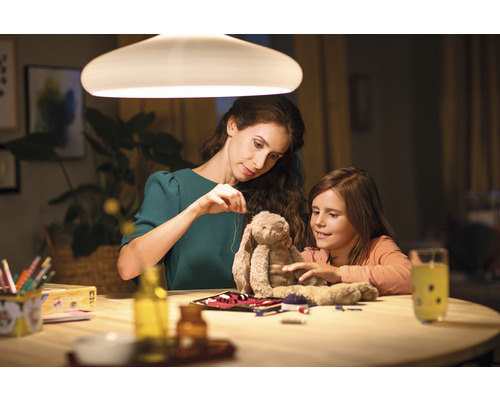 Mutter und Tochter sitzen an einem Tisch und flicken ein Stofftier unter einer Lampe.