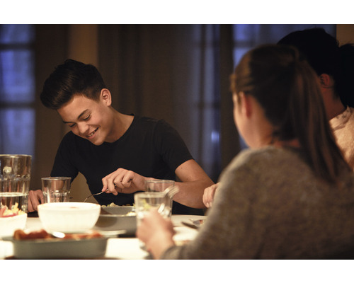 Personen sitzen an einem Esstisch und essen Mahlzeiten aus Schüsseln