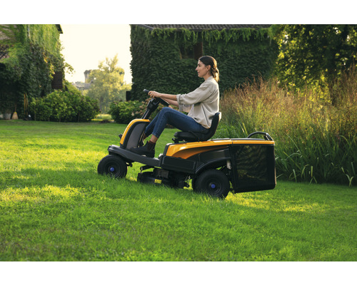 Frau fährt Rasentraktor auf Rasenfläche