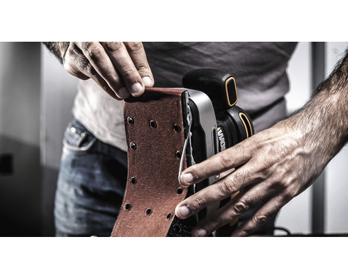 Eine Person wechselt Schleifpapier an einem Bandschleifer.