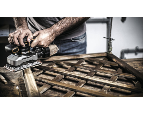 Eine Person schleift mit einem Schwingschleifer ein Holzgitter.