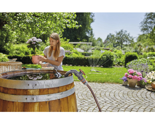 Garten mit Regentonne aus Holz, Wasserhahn und Frau mit Blume