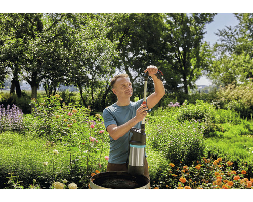Ein Mann bedient eine Regenfasspumpe im Garten.