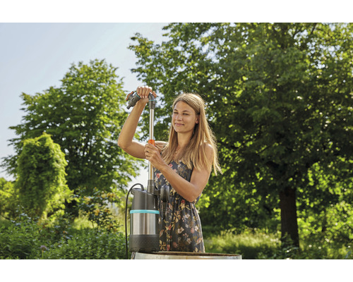 Frau montiert eine Regentonnenpumpe im Garten.