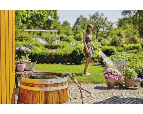 Regenwassertonne aus Holz im Garten, eine Frau gießt Pflanzen