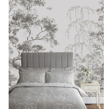 Schlafzimmer mit Bett vor einer Tapete mit Baum- und Vogelmotiven.