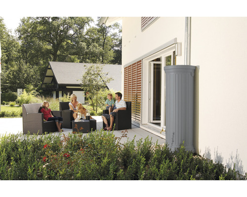Familie sitzt auf der Terrasse neben einem grauen Regenspeicher am Haus
