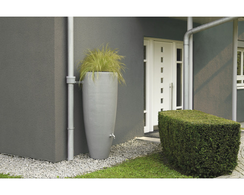 Regenspeicher mit Wasserhahn und bepflanztem Oberteil neben einem Haus