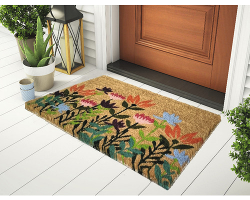 Fußmatte aus Kokosfaser mit Blumenmuster vor einer Haustür.