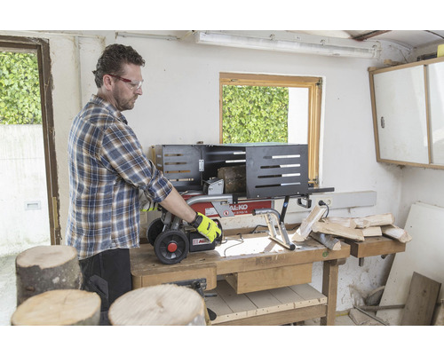 Mann bedient einen Holzspalter auf einer Werkbank, um Holz zu spalten.