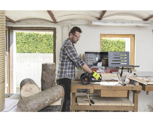 Ein Mann arbeitet mit einem Holzspalter in einer Werkstatt. Holzscheite liegen auf dem Tisch.