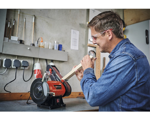 Mann schleift Holzstück an einem Bandschleifer von Einhell in einer Werkstatt.