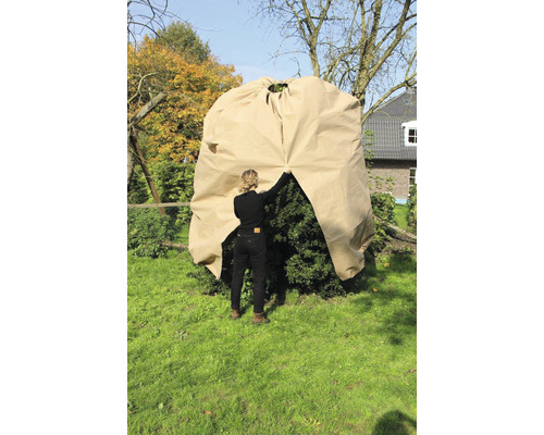 Eine Frau deckt im Garten einen Busch mit einer Pflanzenhaube ab.