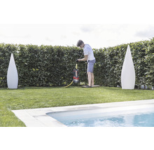 Ein Mann bedient eine Schmutzwasserpumpe in einem Garten nahe einem Pool, flankiert von zwei Deko-Leuchten.