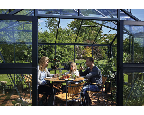 Familie sitzt an einem Tisch in einem Gewächshaus mit Glaswänden.