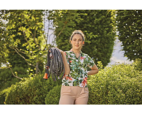 Frau hält einen Gartenschlauch in einem Garten.