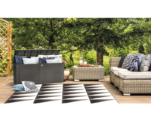 Szene im Garten mit einer Auflagenbox, einem Tisch, einem Sofa und einem Teppich auf einer Holzterrasse
