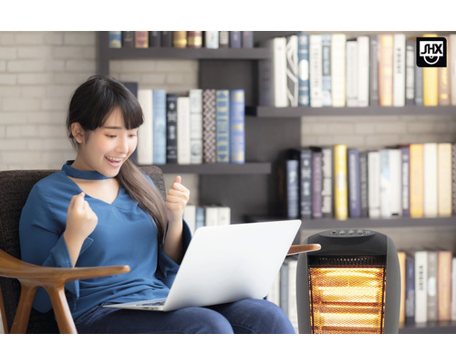 Frau sitzt mit Laptop neben einem Heizlüfter vor einem Bücherregal.