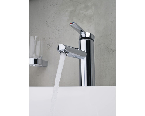 Verchromter Waschtischmischer mit Wasserstrahl und Glasablage im Badezimmer.