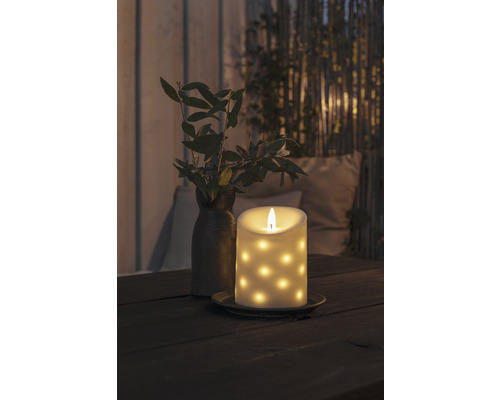 Dekorative LED-Kerze mit Punktmuster auf einem Tisch, neben einer Vase mit Zweigen.