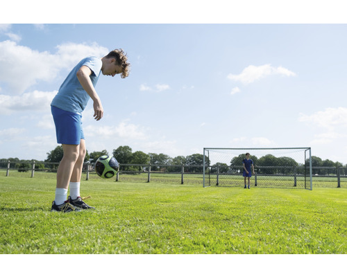 Jugendlicher jongliert Fußball auf einem Fußballplatz.