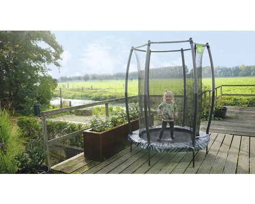 Kleines Mädchen springt auf einem runden Gartentrampolin mit Sicherheitsnetz auf einer Terrasse.