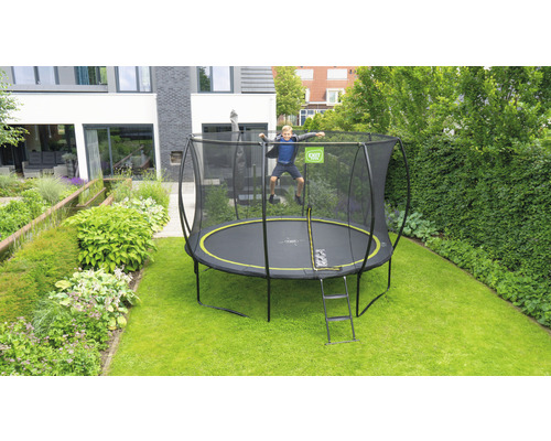 Junge springt auf einem schwarzen Gartentrampolin mit Sicherheitsnetz und Leiter im Garten.