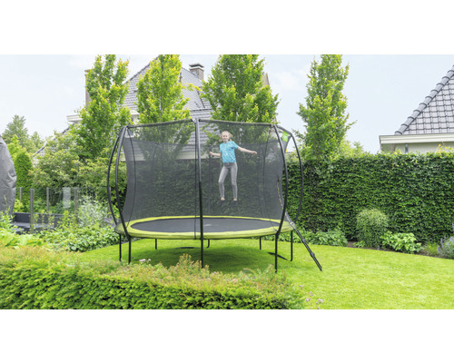 Ein Mädchen springt auf einem Gartentrampolin mit Sicherheitsnetz in einem begrünten Garten.