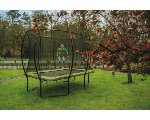 Junge springt auf rechteckigem Gartentrampolin mit Sicherheitsnetz auf Rasenfläche.