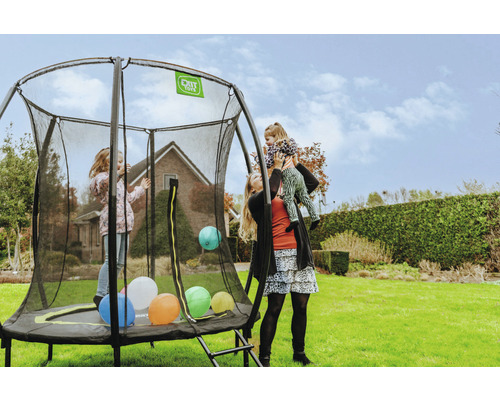 Trampolin mit Sicherheitsnetz im Garten mit spielenden Kindern und einer Frau, die ein Kind auf ihren Schultern trägt