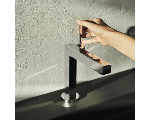 Eine Hand bedient einen verchromten Wasserhahn im Badezimmer.