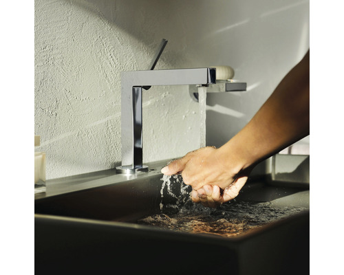 Person wäscht sich die Hände unter einem verchromten Wasserhahn in einem Badezimmerwaschbecken