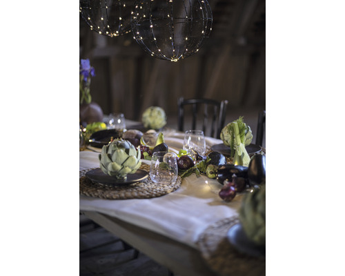 Festlich gedeckter Tisch mit Kugelleuchten, Geschirr, Gläsern und saisonalem Gemüse als Dekoration.