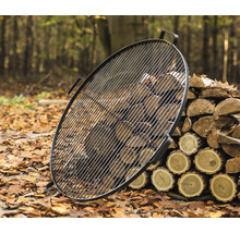 Runder Grillrost aus Metall mit Holzstapel im Freien