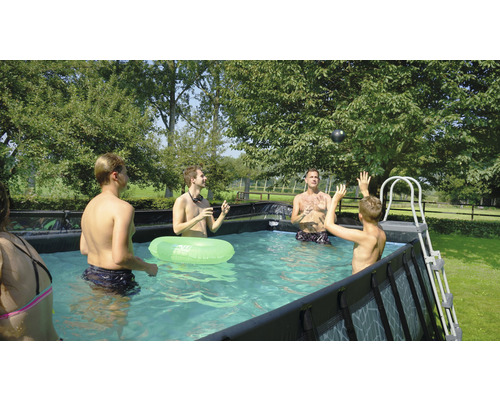 Familie spielt im Aufstellpool mit Ball und Schwimmring im Garten.
